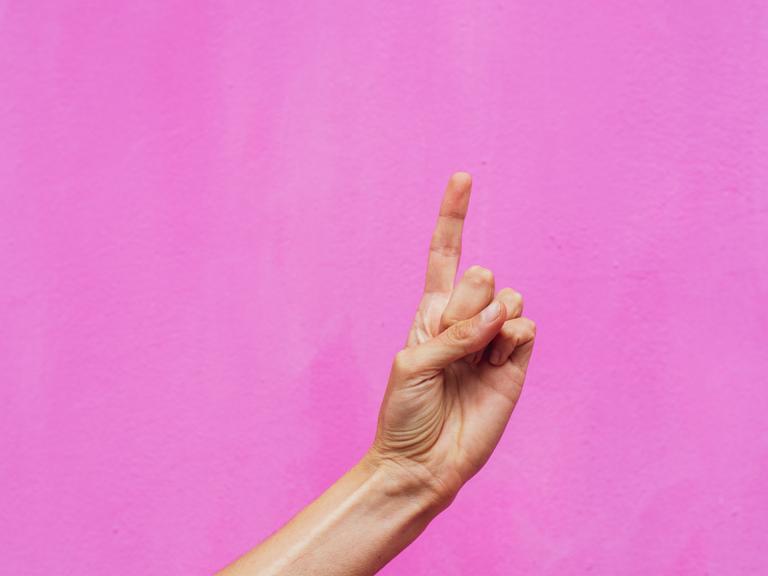 Ein erhobener Zeigefinger vor pinkem Hintergrund.