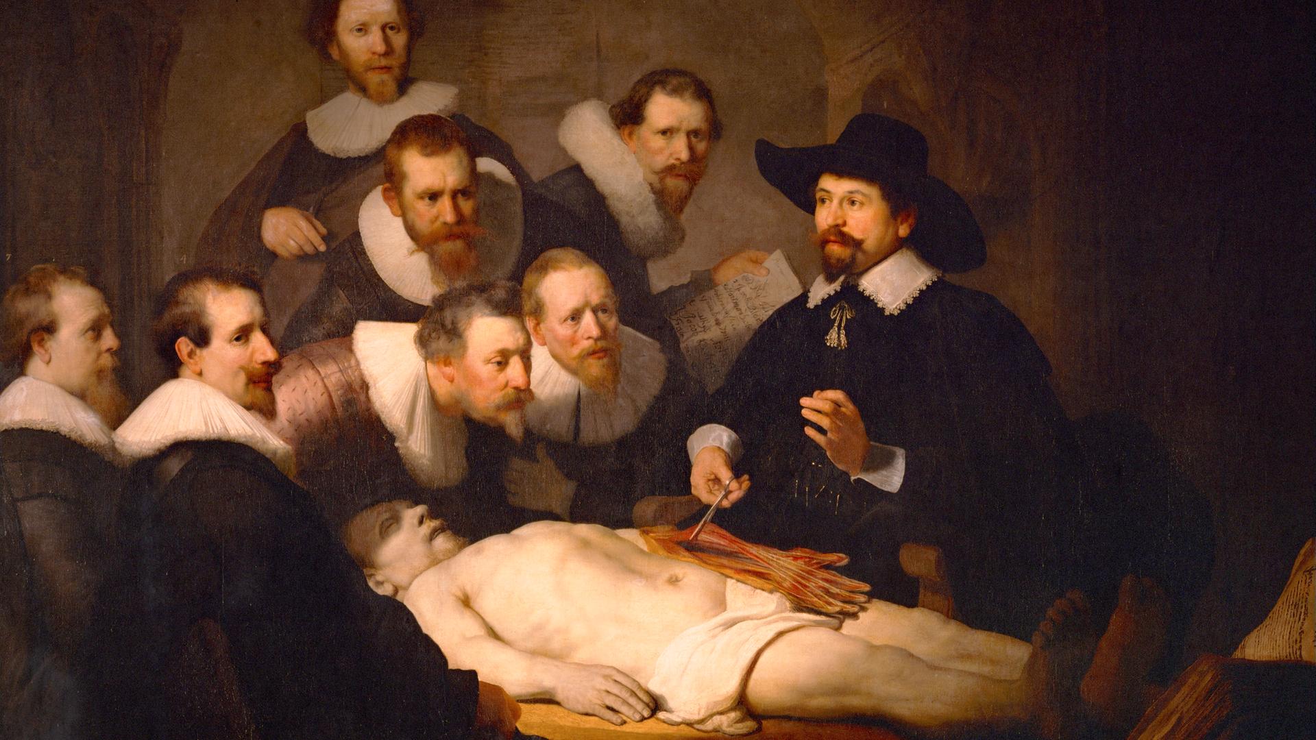 Das Bild zeigt das Gemälde "Die Anatomie des Dr. Tulp" vom niederländischen Maler Rembrandt aus dem Jahr 1631. Darauf sind insgesamt acht Männer abgebildet, die sich um eine Leiche versammelt habe. Diese wird zu wissenschaftlichen Zwecken untersucht.