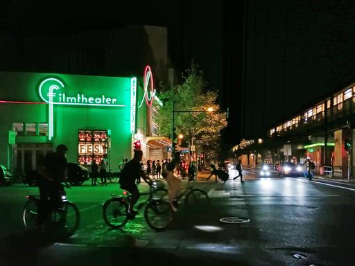 Nachtansicht eines großen Kinogebäudes auf dem in grünen Neonlettern das Wort "Filmtheater" steht