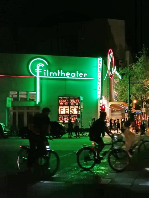 Nachtansicht eines großen Kinogebäudes auf dem in grünen Neonlettern das Wort "Filmtheater" steht