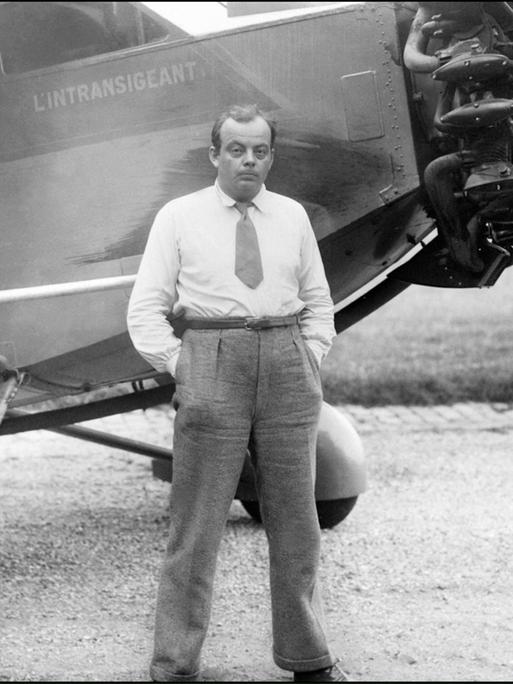 Der französische Autor und Pilot Antoine de Saint-Exupéry steht vor seinem Flugzeug, die Hände in den Hosentaschen.