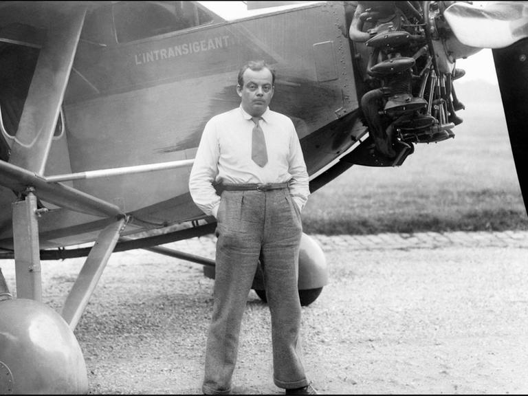 Der französische Autor und Pilot Antoine de Saint-Exupéry steht vor seinem Flugzeug, die Hände in den Hosentaschen.