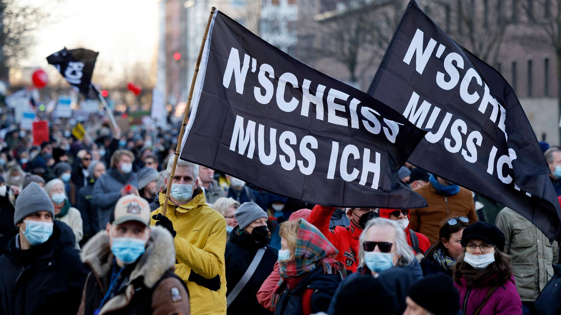 Menschen demonstrieren gegen Coronamaßnahmen und tragen schwarze Fahnen mit der Aufschrift „N’SCHEISS MUSS ICH“.