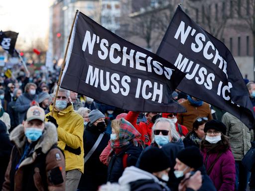 Menschen demonstrieren gegen Coronamaßnahmen und tragen schwarze Fahnen mit der Aufschrift „N’SCHEISS MUSS ICH“.