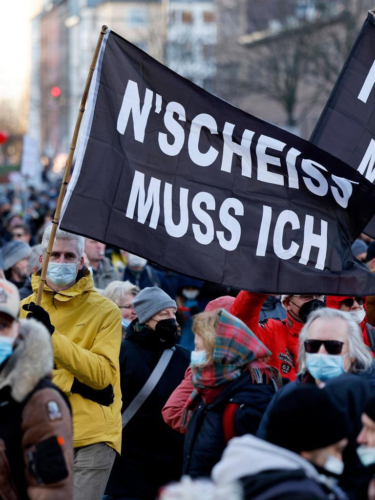 Menschen demonstrieren gegen Coronamaßnahmen und tragen schwarze Fahnen mit der Aufschrift „N’SCHEISS MUSS ICH“.