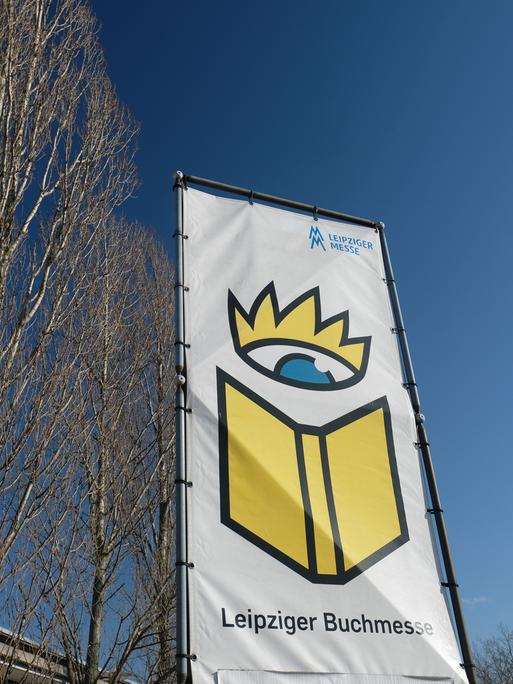 Ein Banner mit der Aufschrift "Leipziger Buchmesse" und einem gemalten Buch unter einer gemalten Krone flattert im Wind. 