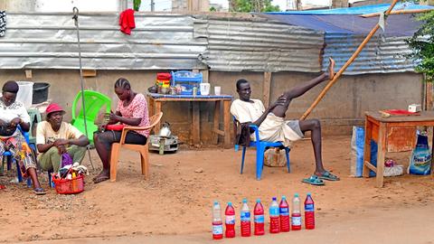 Strassenhändler in der südsudanesischen Hauptstadt Dschuba, ein junger Mann, der Benzin in Trinkwasserflaschen in kleineren Portionierungen verkauft, hat es sich bequem gemacht und ein Bein auf eine Stange abgestützt, 2021.