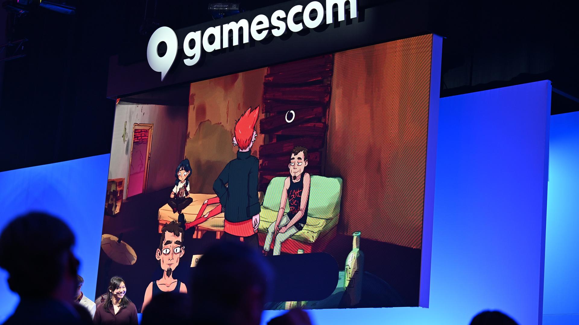 Bei der politischen Eröffnung der Gamescom blicken Zuschauer in Richtung Bühne, während auf einer Leinwand Szenen des Computerspiels "Grenzgänger" gezeigt werden. 