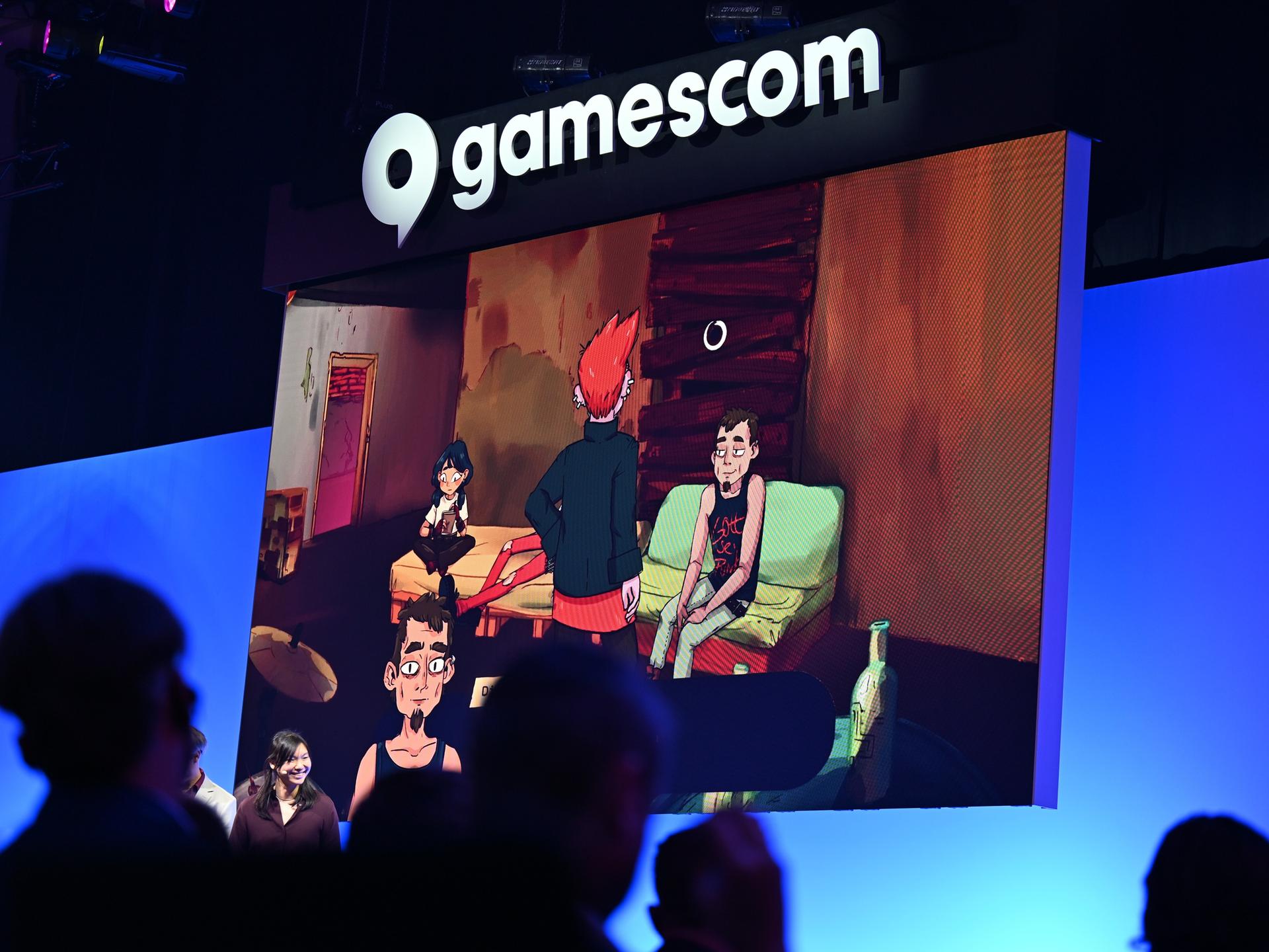 Bei der politischen Eröffnung der Gamescom blicken Zuschauer in Richtung Bühne, während auf einer Leinwand Szenen des Computerspiels "Grenzgänger" gezeigt werden. 