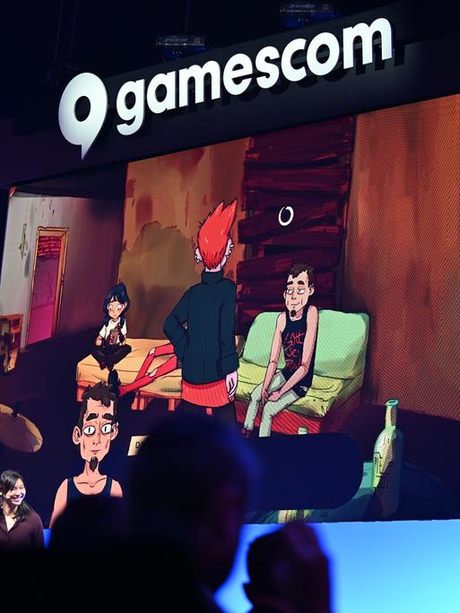 Bei der politischen Eröffnung der Gamescom blicken Zuschauer in Richtung Bühne, während auf einer Leinwand Szenen des Computerspiels "Grenzgänger" gezeigt werden. 