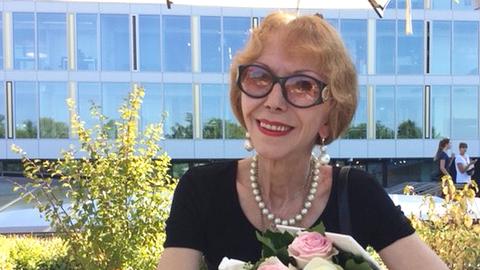 Rosemarie Schubert-Blum. Eine ältere Frau mit halblangen Haaren und Sonnenbrille sitzt auf der Terrasse eines Kaffees. 