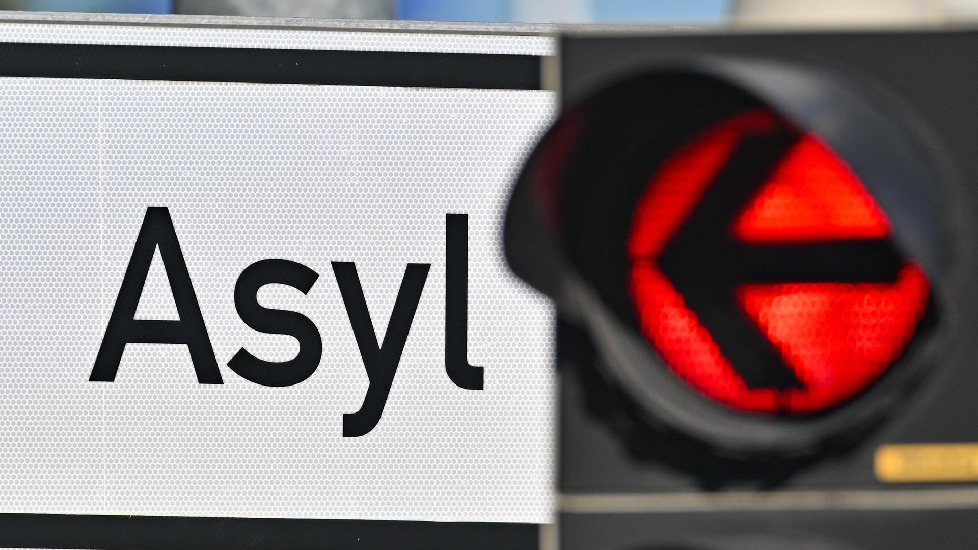 Eine rote Ampel leuchtet vor dem Wort "Asyl" auf einem Wegweiser.