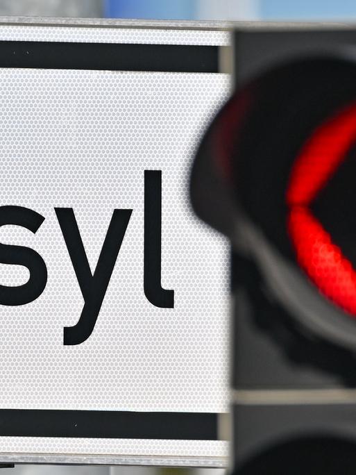 Eine rote Ampel leuchtet vor dem Wort "Asyl" auf einem Wegweiser. Eine rote Ampel leuchtet vor dem Wort "Asyl" auf einem Wegweiser.
