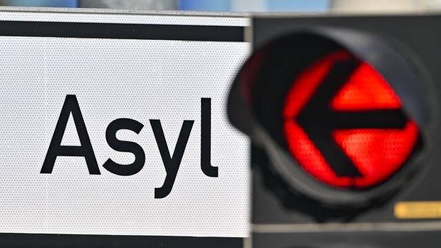 Eine rote Ampel leuchtet vor dem Wort "Asyl" auf einem Wegweiser.