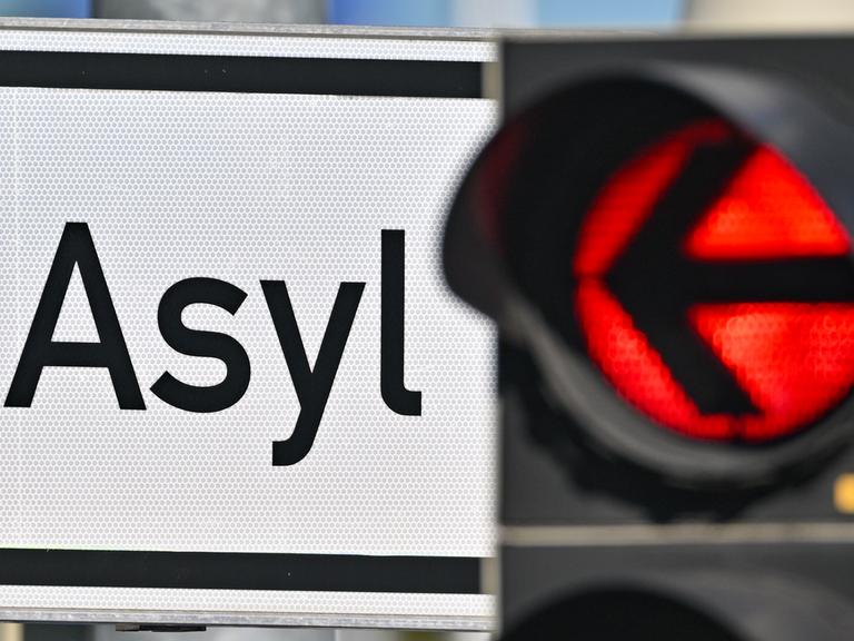Eine rote Ampel leuchtet vor dem Wort "Asyl" auf einem Wegweiser. Eine rote Ampel leuchtet vor dem Wort "Asyl" auf einem Wegweiser.