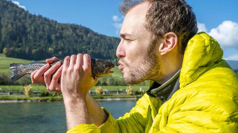 Ein Mann hält einen Fisch vor sein Gesicht und deutet einen Kuss an.