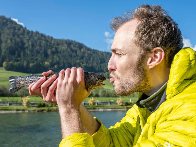 Ein Mann hält einen Fisch vor sein Gesicht und deutet einen Kuss an.