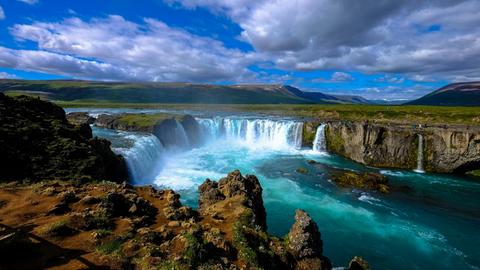 Blick auf einen großen isländischen Wasserfall mit blauem Himmel und wilden Wolken. Blick auf einen großen isländischen Wasserfall mit blauem Himmel und wilden Wolken.