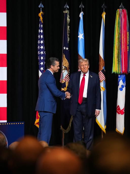 Präsident Donald Trump schüttelt "Kriegsminister "Pete Hegseth"auf einer Bühne die Hand. Aufnahmedatum: 30. September 2025