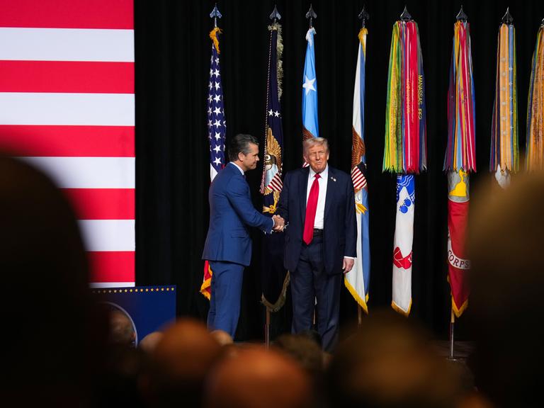 Präsident Donald Trump schüttelt "Kriegsminister "Pete Hegseth"auf einer Bühne die Hand. Aufnahmedatum: 30. September 2025