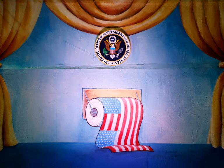 Zu sehen ist eine Klorolle mit der Flagge der Vereinigten Staaten von Amerika beim Richtfest der Persiflage- und Motivwagen zum Kölner Rosenmontagszug 2023 in der Koelnmesse.