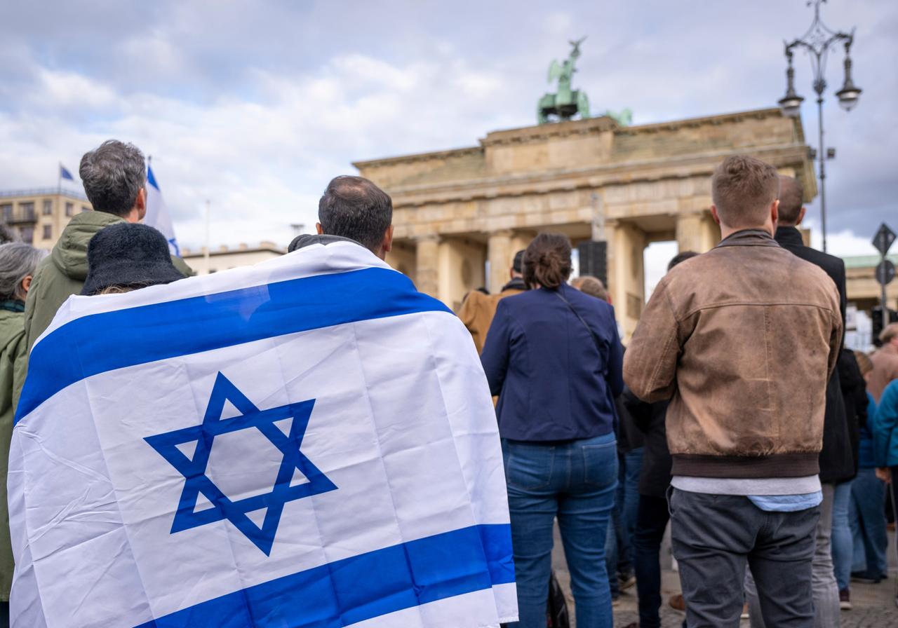 Teilnehmer der Kundgebung "Aufstehen gegen Terror, Hass und Antisemitismus" im Oktober sind von hinten zu sehen mit Blick auf das Brandenburger Tor in Berlin. Einige von ihnen sind eingehüllt in eine israelische Flagge.