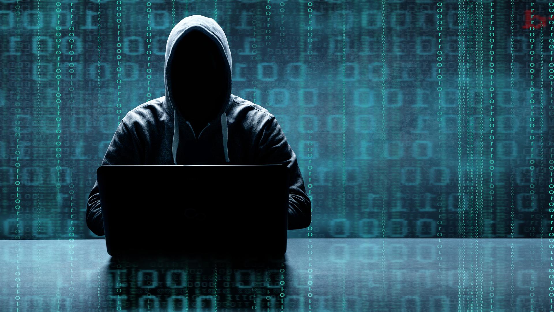 Hacker, ein Mann mit schwarzer Kapuze vor einem Laptop Hacker, ein Mann mit schwarzer Kapuze vor einem Laptop