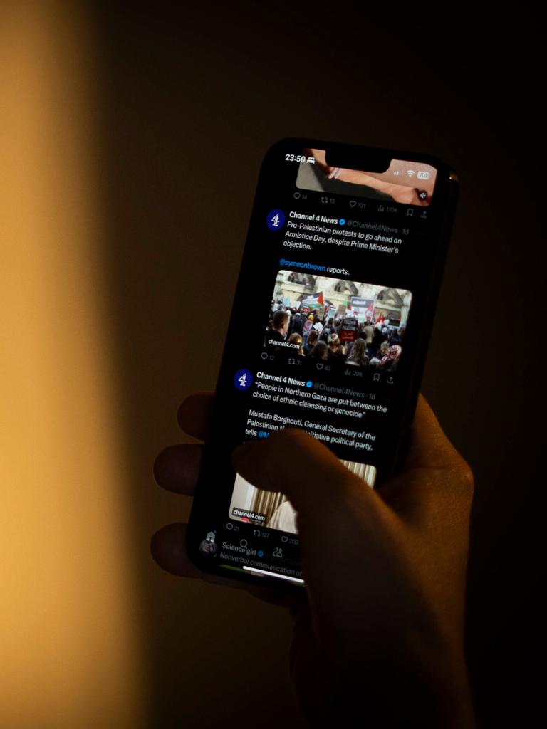 Ein Mensch mit Brille hält ein Smartphone in der Hand und schaut darauf. Auf dem Bildschirm ist die Online-Plattform X geöffnet. 