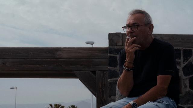 Ein Mann sitzt am Strand und zieht sinnierend an einer Zigarette