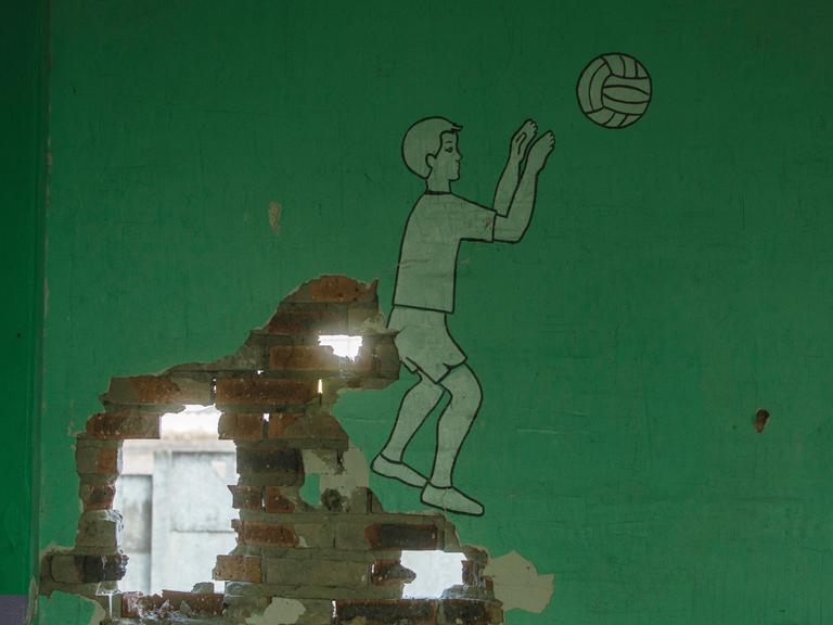 Eine durch militärischen Beschuss durchlöcherte Wand in einer Schule in Bakhmut, Gebiet Donezk. Auf der grünen Wand ist ein Junge beim Ball spielen abgebildet.