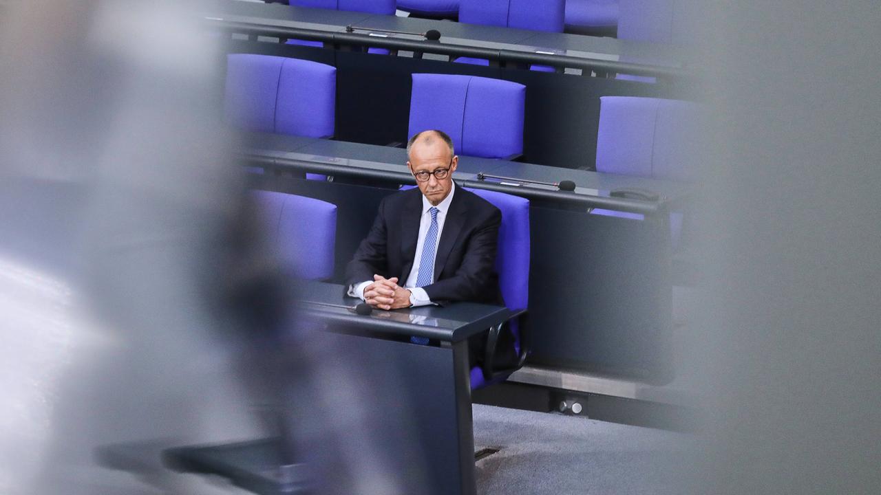 Bundeskanzler Friedrich Merz sitzt allein mit einem ernsten Gesicht auf einem blauen Stuhl im Bundestag.