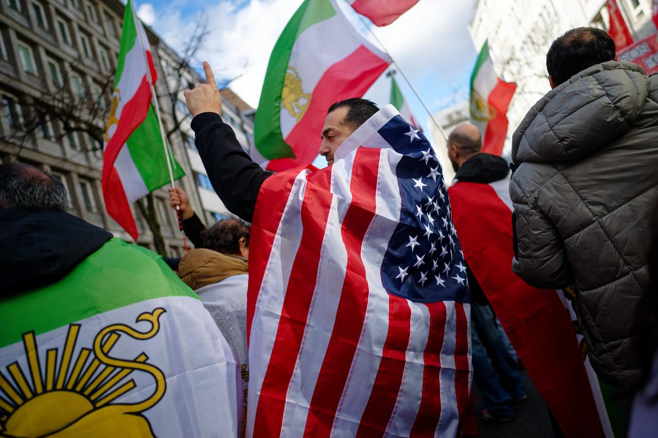 Teilnehmer einer Demonstration gegen das iranische Mullah-Regime in Düsseldorf feiern den Tod des obersten Führer des Irans, Ajatollah Chamenei. Ein Mann hat sich dabei in eine US-Flagge gehüllt.