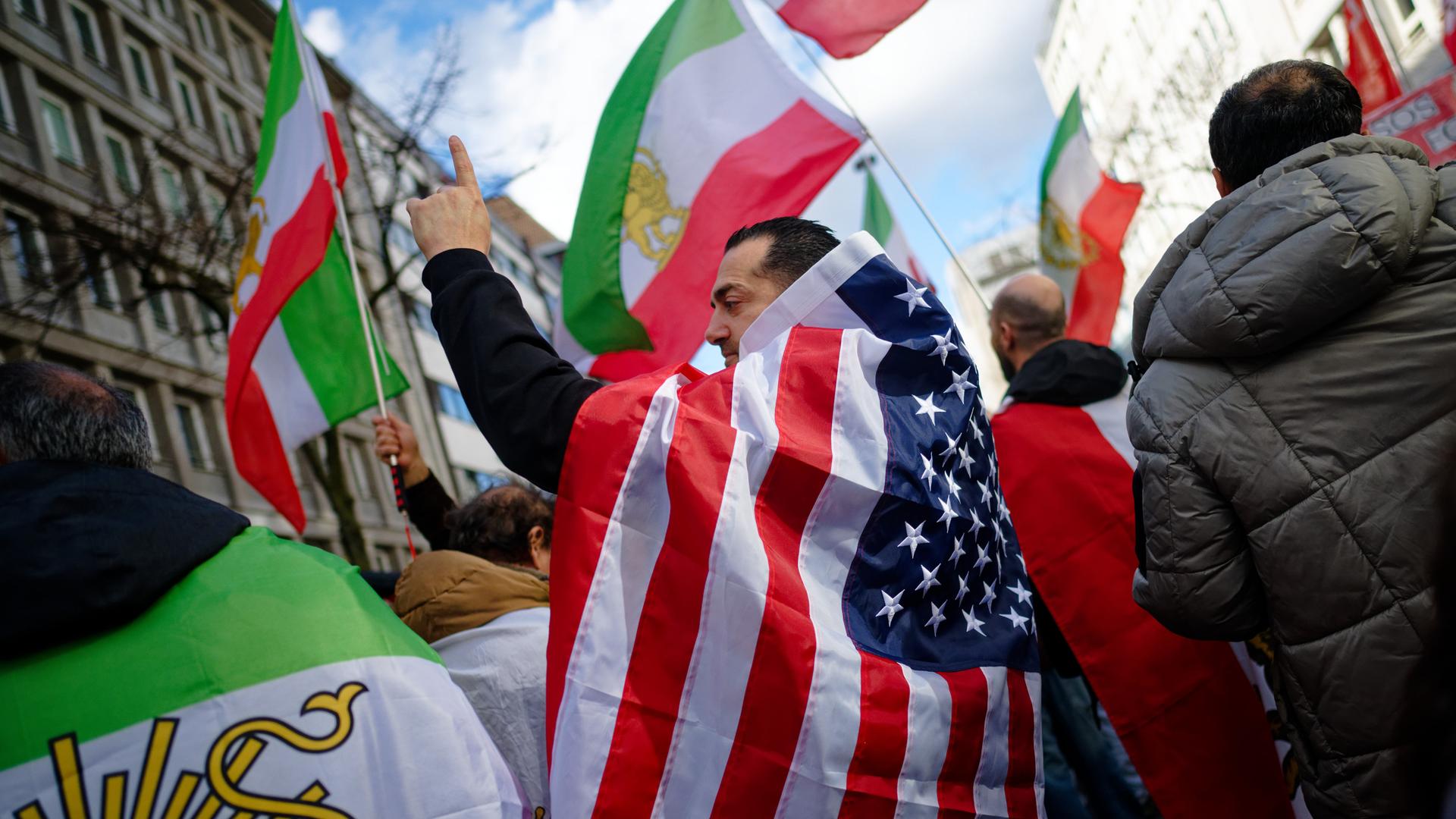 Teilnehmer einer Demonstration gegen das iranische Mullah-Regime in Düsseldorf feiern den Tod des obersten Führer des Irans, Ajatollah Chamenei. Ein Mann hat sich dabei in eine US-Flagge gehüllt. Teilnehmer einer Demonstration gegen das iranische Mullah-Regime in Düsseldorf feiern den Tod des obersten Führer des Irans, Ajatollah Chamenei. Ein Mann hat sich dabei in eine US-Flagge gehüllt.