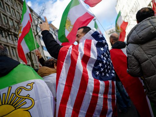 Teilnehmer einer Demonstration gegen das iranische Mullah-Regime in Düsseldorf feiern den Tod des obersten Führer des Irans, Ajatollah Chamenei. Ein Mann hat sich dabei in eine US-Flagge gehüllt.