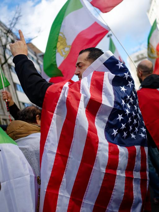 Teilnehmer einer Demonstration gegen das iranische Mullah-Regime in Düsseldorf feiern den Tod des obersten Führer des Irans, Ajatollah Chamenei. Ein Mann hat sich dabei in eine US-Flagge gehüllt.