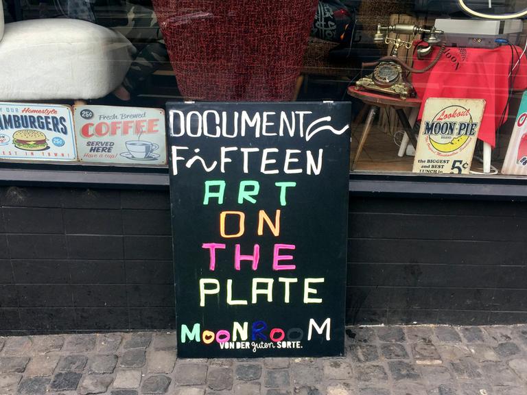 Auf einem Aufsteller steht in bunter Schrift: "Documenta Fifteen - Art on the Plate".