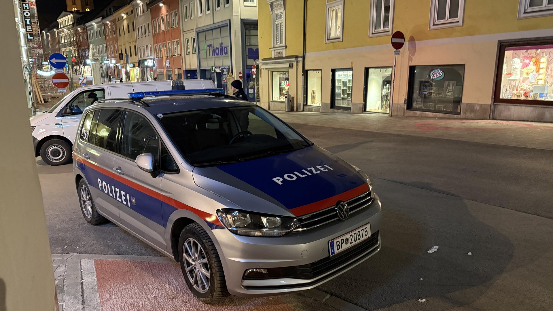 Das Bild zeigt eine Straßenszene in Villach nach einer Messerattacke. Im Vordergrund steht ein Polizeifahrzeug. 