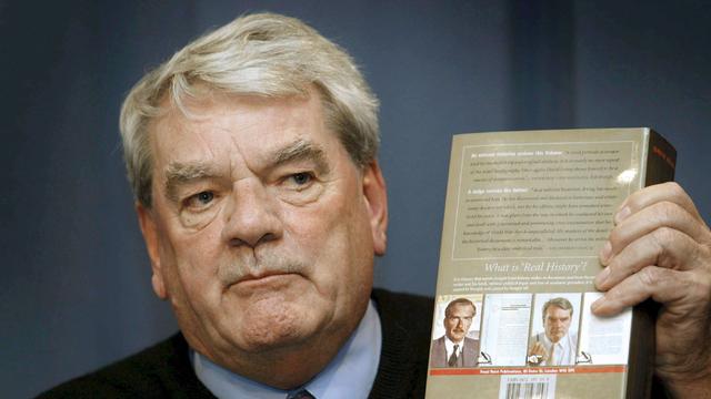 Ein Mann hält ein Buch nach oben, auf dem die Frage zu lesen ist: "What is 'Real History'?"