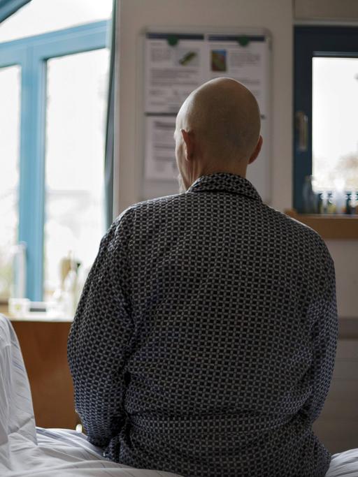 Ein 61 jaehriger Krebspatient im Palliativzentrum der Uniklinik Köln sitzt mit dem Rücken zur Kamera auf seinem Bett und schaut aus dem Fenster.