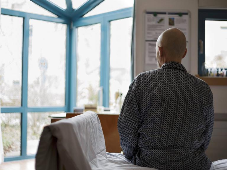 Ein 61 jaehriger Krebspatient im Palliativzentrum der Uniklinik Köln sitzt mit dem Rücken zur Kamera auf seinem Bett und schaut aus dem Fenster.