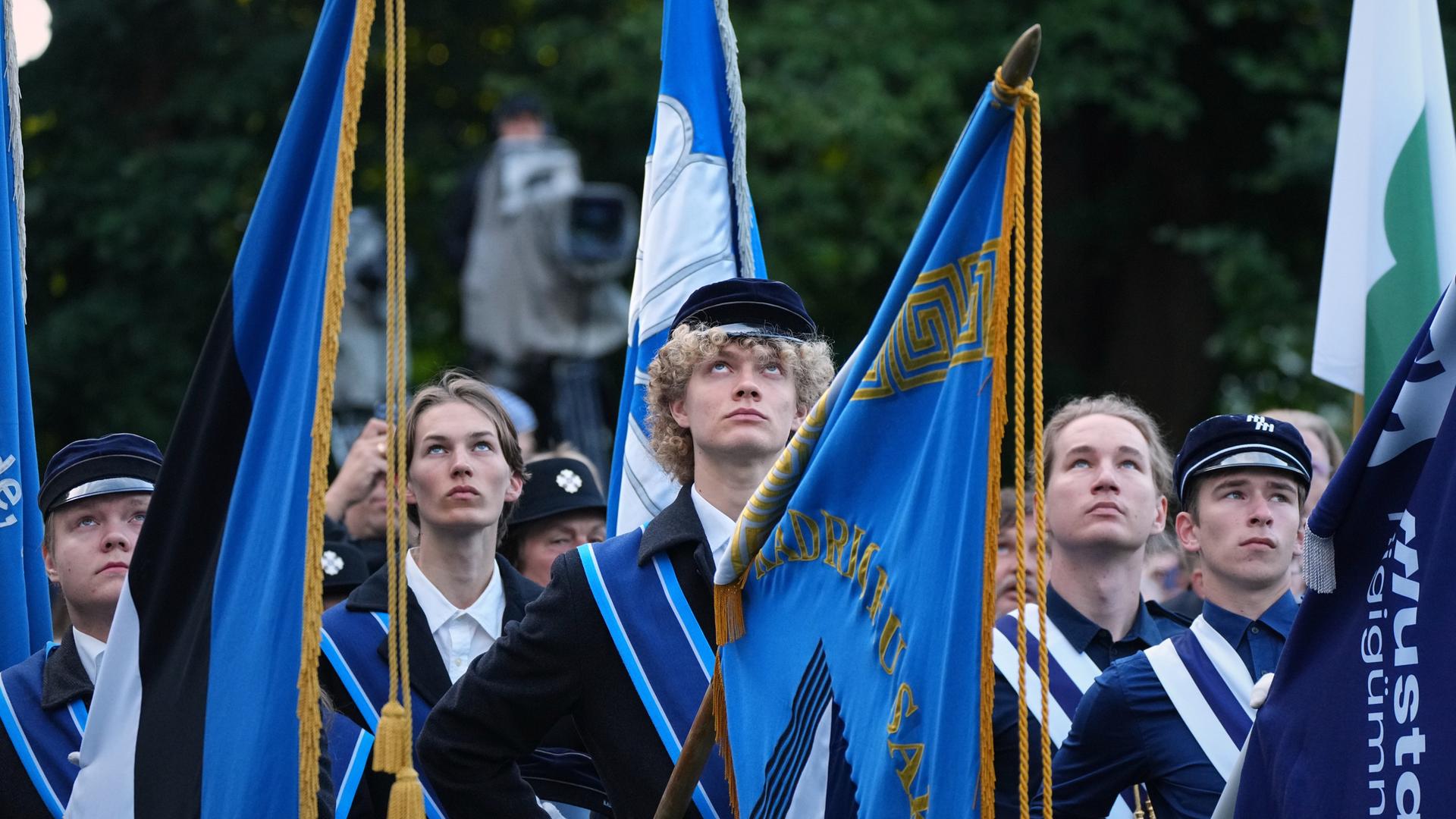 Mehrere junge Esten halten blaue Fahnen in den Händen. Sie schauen nach oben. Mehrere junge Esten halten blaue Fahnen in den Händen. Sie schauen nach oben.