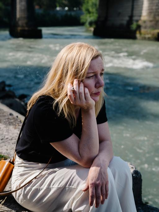 Sandra Hüller als Ingeborg Bachmann sitzt, nachdenklich auf das Wasser schauend und rauchend, am Ufer des Tiber in Rom.