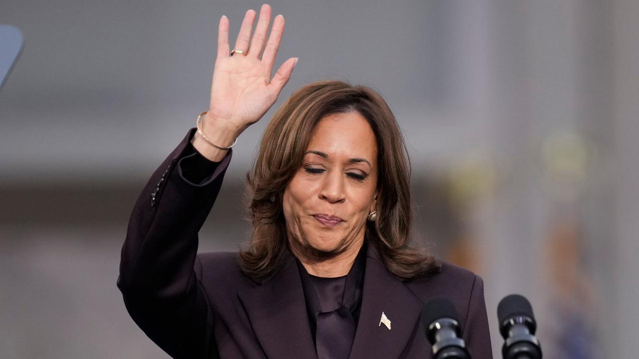 Kamala Harris steht hinter Mikrofonen und winkt. 