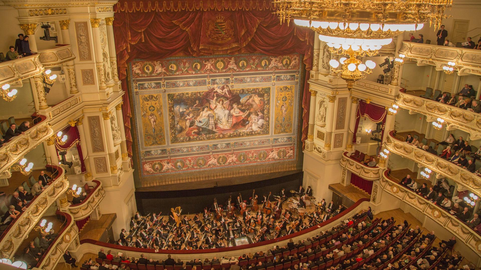 Blick in den Opernsaal der Dresdner Semperoper mit Schmuckvorhang, Kronleuchter, Orchester und Publikum vom oberen Rang aus