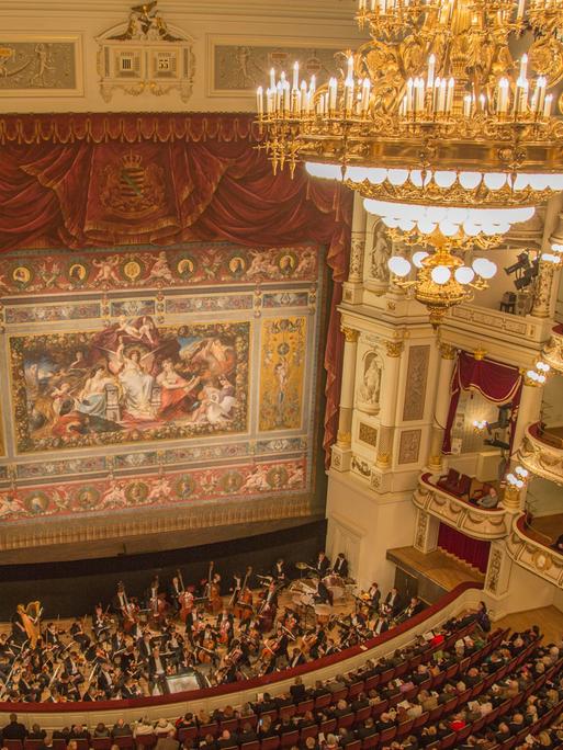 Blick in den Opernsaal der Dresdner Semperoper mit Schmuckvorhang, Kronleuchter, Orchester und Publikum vom oberen Rang aus
