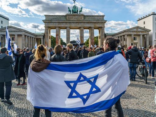 Vor dem Brandenburger Tor sind bei einer Solidaritätsdemo für das von der islamistischen Hamas angegriffene Israel Menschen vor dem Brandenburger Tor in Berlin zusammengekommen. Im Vordergrund tragen zwei Menschen eine Israel-Flagge um die Schulter.