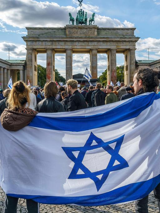 Vor dem Brandenburger Tor sind bei einer Solidaritätsdemo für das von der islamistischen Hamas angegriffene Israel Menschen vor dem Brandenburger Tor in Berlin zusammengekommen. Im Vordergrund tragen zwei Menschen eine Israel-Flagge um die Schulter.