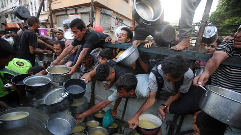 Eine Wohltätigkeitsorganisation verteilt in Gaza-Stadt warme Mahlzeiten an Palästinenser, die eng an eng mit Schüsseln auf das Essen warten. 