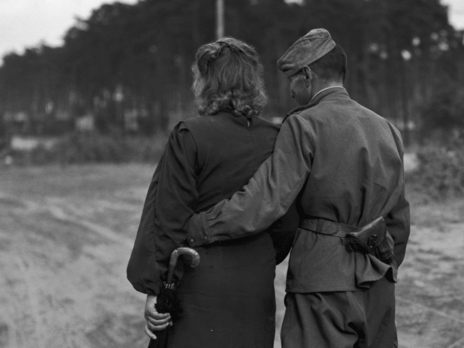 Auf dem schwarz-weiß Bild ist ein Paar von hinten abgebildet. Sie gehen von der Kamera weg. Er trägt eine russische Uniform.