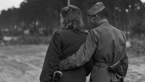 Auf dem schwarz-weiß Bild ist ein Paar von hinten abgebildet. Sie gehen von der Kamera weg. Er trägt eine russische Uniform.
